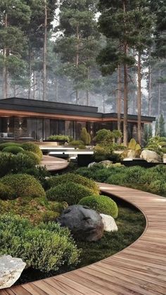 a garden with rocks, grass and trees in front of a house that is surrounded by woods