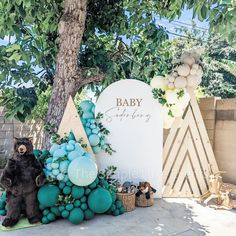 an outdoor baby shower with balloons and decorations on the side of the wall, next to a tree