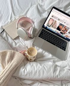 a laptop computer sitting on top of a bed next to headphones and a cup