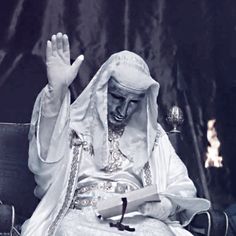 a man sitting in a chair with his hands up and wearing a white robe on