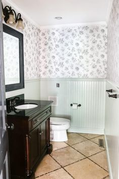 a bathroom with a toilet, sink and mirror in it's corner area next to a wallpapered wall