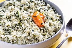 a bowl filled with rice and carrots on top of a yellow table cloth next to a spoon