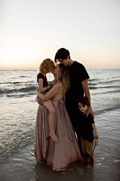 three people standing on the beach with their arms around each other and one person holding a child