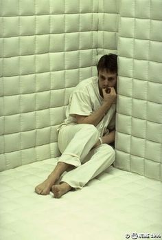 a man sitting on top of a bed talking on a cell phone