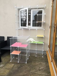 a cat sitting on top of a small cage next to a black couch and window