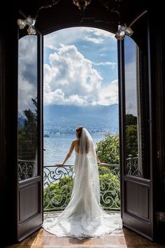 a woman in a wedding dress is looking out an open door at the ocean and mountains