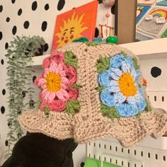 a crocheted hat with flowers on it sitting on a shelf in a room