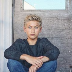 a young man sitting on the ground in front of a door with his arms crossed