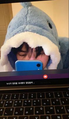 a person in a shark costume looking at a cell phone on a laptop computer screen