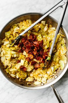 a bowl filled with cabbage and bacon next to two tongs