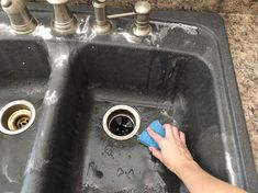 a person cleaning a black sink with a blue rag on the side and two faucets