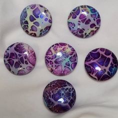 five purple and blue glass cabochons sitting on top of a white cloth covered table