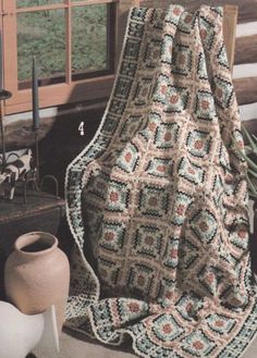 a crocheted blanket sitting on top of a table next to a vase