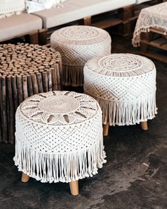 three white stools with tassels on them sitting in front of a couch