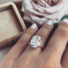 a close up of a person's hand with a ring on it and a rose in the background