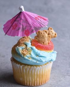 a cupcake with blue frosting and a teddy bear on top has an umbrella