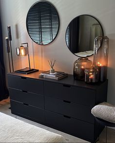 two round mirrors on the wall above a dresser with candles and books in front of it