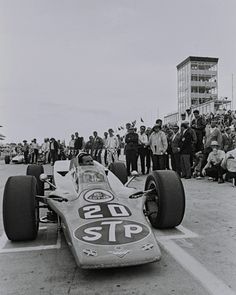 an old photo of a race car on the track with people standing around looking at it