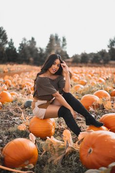 a woman sitting on top of pumpkins in a field with her cell phone to her ear