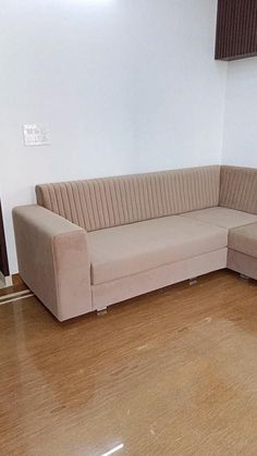 a beige couch sitting on top of a hard wood floor next to a white wall