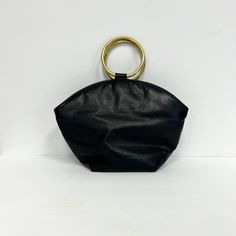 "Vintage 1970s leather bucket bag featuring; top handles that are gold metal o rings curved top edge zippered top  single compartment with small zippered coin pocket flat bottom doubles as a cross body bag with a clip on long leather strap of a soft, supple black leather, the lining appears to be black vinyl, all metal hardware is gold labeled \"Park Avenue Int. Genuine Leather, Made in the U.S.A.\", measurements are  10 1/4 inches wide at the widest point 4 1/2 inches wide at the bottom 8 inche Gold Bucket Bag With Metal Hardware For Everyday Use, Chic Bucket Bag With Brass Hardware Tote, Chic Bucket Bag Tote With Brass Hardware, Chic Tote Bucket Bag With Brass Hardware, Vintage Gold Bag With Metal Hardware, Vintage Gold Bags With Metal Hardware, Vintage Bucket Bag With Detachable Handle, Vintage Bucket Bag With Detachable Handle For Everyday, Ring Der O