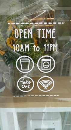 there is a sign that says open time on the front window and flowers behind it