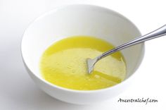 a white bowl filled with yellow liquid and a spoon