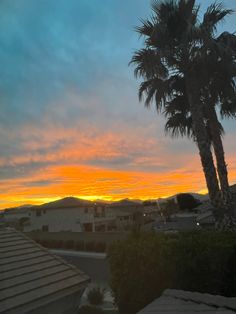 the sun is setting over some houses and palm trees in front of a mountain range