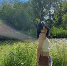 a woman is standing in the grass near water