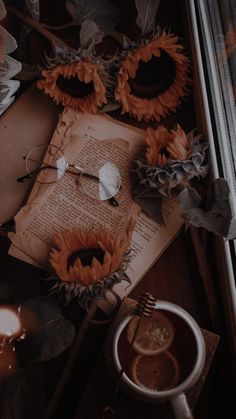 an open book with sunflowers on it next to a cup of coffee and candles