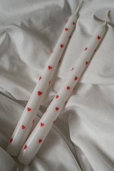 two white candles with red hearts on them are laying on a bed sheet and cover