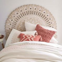 a white bed topped with lots of pillows next to a wall mounted headboard and night stand