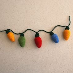 knitted christmas lights are hanging on a string with green and red balls attached to them