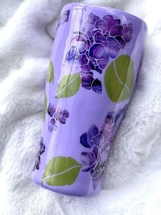 a purple vase with flowers on it sitting on a white blanket next to a cell phone