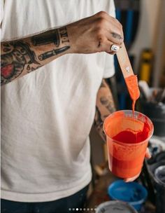 a man is pouring red liquid into a plastic cup with a wooden stick in his hand