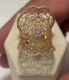 a gold and diamond ring sitting on top of a white display case in someone's hand