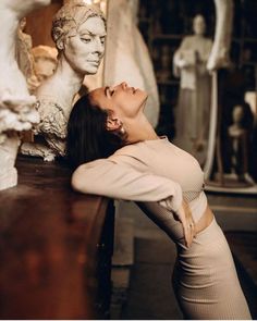 a woman laying on top of a wooden table next to a white busturine