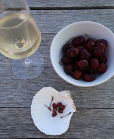 a bowl of cherries next to a glass of white wine on a wooden table