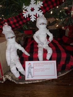 two paper mache dolls sitting under a christmas tree