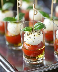 small glasses filled with mozzarella and tomato on a metal tray, topped with toothpicks