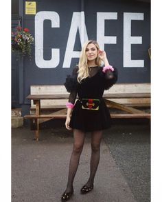 a woman standing in front of a cafe sign with her hands on her head and wearing black tights