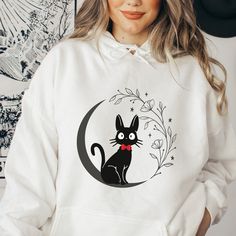 a woman wearing a white hoodie with a black cat on the moon printed on it