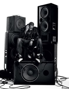 a man sitting on top of speakers with his hands to his face while talking on the phone