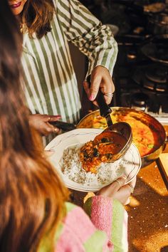 two women are serving themselves food at a buffet table with plates and pans on it