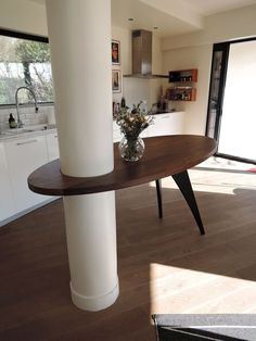 a vase with flowers sitting on top of a wooden table in a kitchen next to a window