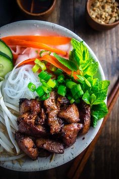 a white bowl filled with meat and veggies next to chopsticks on a wooden table