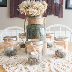 mason jars filled with flowers and rocks on a doily covered table in front of a window