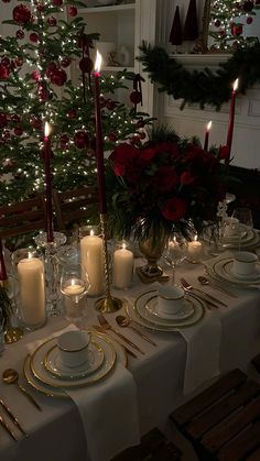 a table set for christmas dinner with lit candles and plates in front of a decorated christmas tree