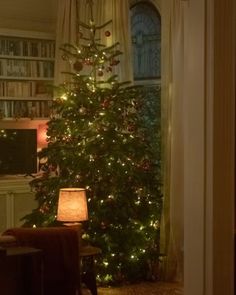 a living room with a lit christmas tree in the corner and a chair next to it