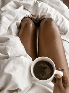 a woman laying in bed holding a cup of coffee